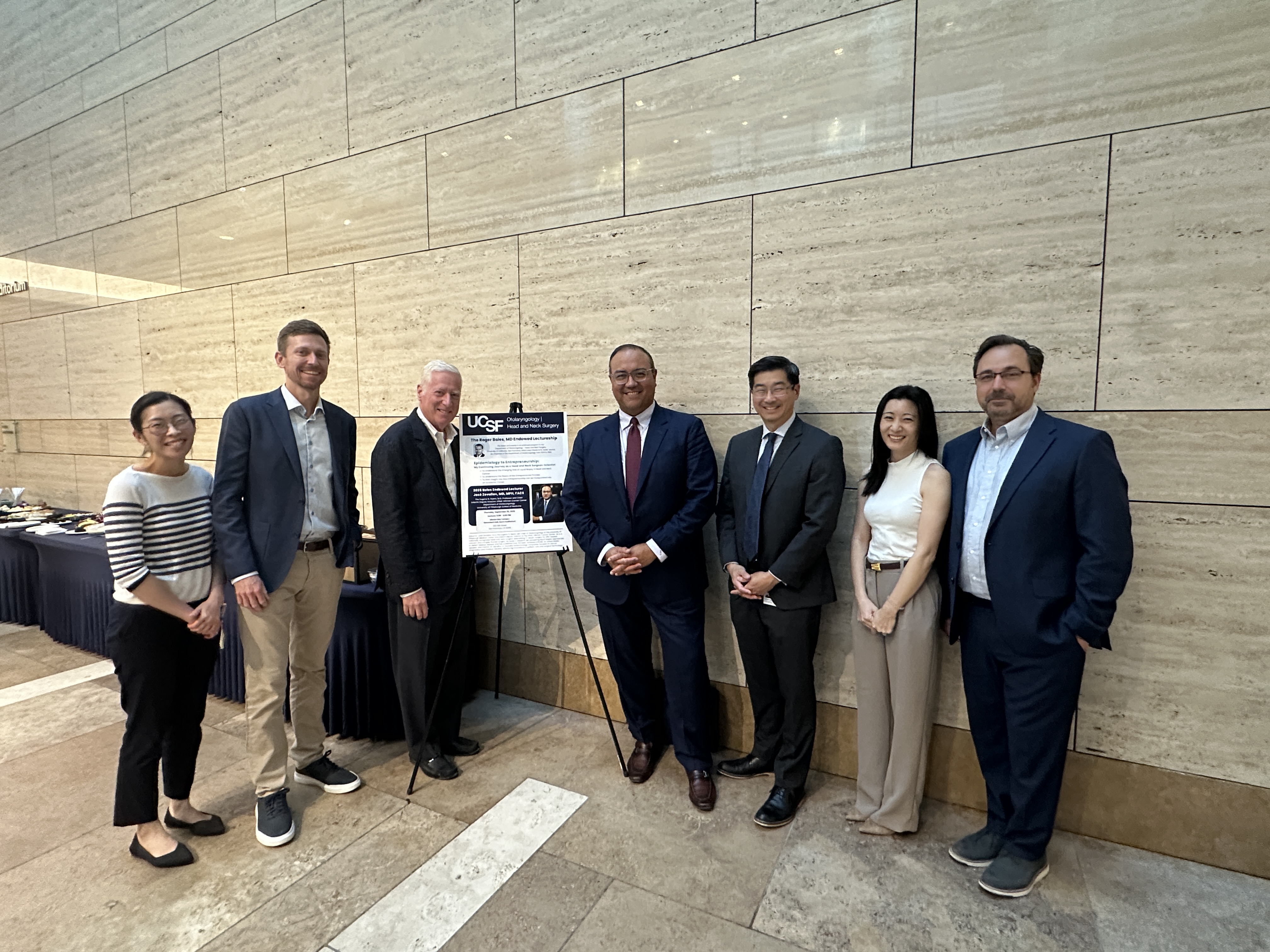 Dr. Zevallos and Dr. Murr stand in a group of other attendees of the Boles Lectureship, posing by the event banner.